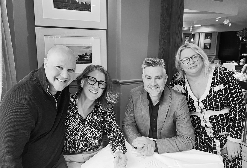 Group of colleagues gathered around a table at an indoor event, posing together in a social or professional setting.